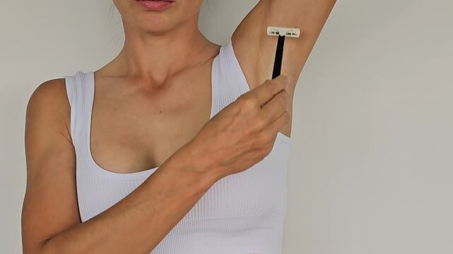 Woman shaving her armpit with a razor on a dark white background