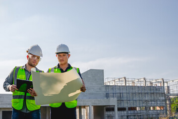 Two construction engineers inspect the progress of a building construction plan at a construction site.