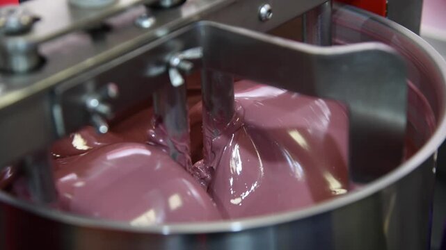 Close-up view of working of modern rotary conche machine. Stirring machine mixes ruby chocolate mass. Real time handheld video. Soft focus. Confectionery production theme.