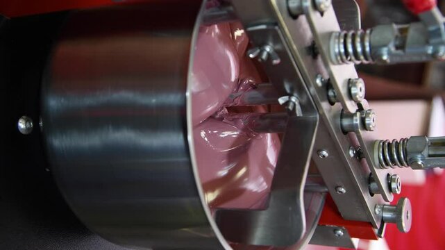 Close-up view of working of modern rotary conche machine. Stirring machine mixes ruby chocolate mass. Real time handheld vertical video. Soft focus. Confectionery production theme.