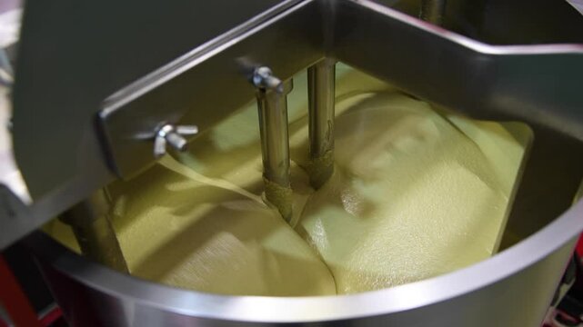 Close-up view of working of modern rotary conche machine. Stirring machine mixes white chocolate mass. Real time handheld video. Soft focus. Confectionery production theme.