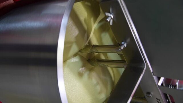 Close-up view of working of modern rotary conche machine. Stirring machine mixes white chocolate mass. Real time handheld vertical video. Soft focus. Confectionery production theme.