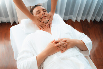 Caucasian man enjoying relaxing anti-stress head massage and pampering facial beauty skin recreation leisure in dayspa modern light ambient at luxury resort or hotel spa salon. Quiescent