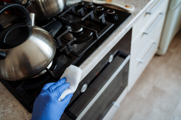 A person is wearing blue gloves while effectively cleaning a stove with a cloth, ensuring it is free from dirt and grime for a spotless kitchen surface and a better cooking experience