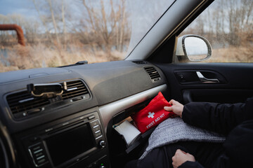 A person is seated comfortably inside a car, clutching a vibrant and easily identifiable bright red first aid kit, prepared to assist anyone in need during an emergency situation