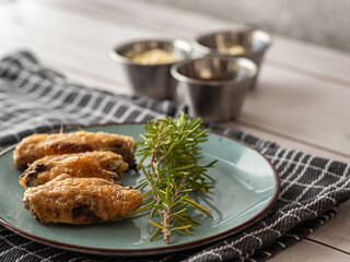 Plate of fried chicken wings decorated with rosemary and accompanied by three sauces on table cloth on white wooden table