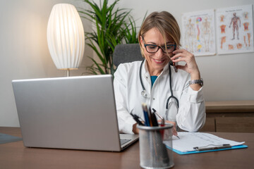 Female doctor talking with colleagues with smartphone  with a laptop in the consultation. Female...