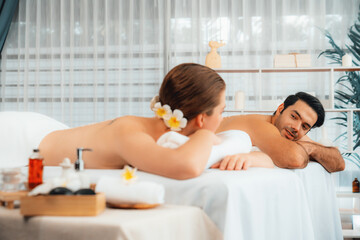 Blissful couple customer having exfoliation treatment in luxury spa salon with warmth candle light ambient. Salt scrub beauty treatment in health spa body scrub. Quiescent