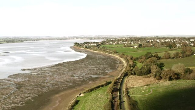 Aerial view of the south coast of England Devon landscape as train travels along the exe river. Drone flying high with rail travel along scenic landscape UK 4K