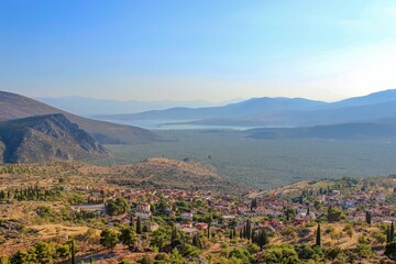 A scenic view with sprawling olive groves, distant mountains, and serene waters under a clear sky, showcasing the region's natural beauty.