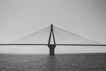 Black and white image of a suspension bridge over calm waters, showcasing its sleek architectural...
