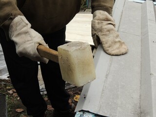 A worker wearing construction gloves and bending or straightening a metal sheet with a wooden...