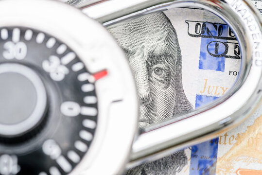 Financial or cyber security, fraud prevention, safeguarding assets and secure transactions : A combination of a US 100 dollar bill featuring Benjamin Franklin partially obscured by a combination lock.