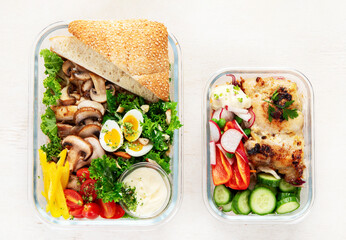 Lunch box containers with grilled chicken breast and fresh vegetable salad.