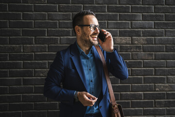 adult businessman stand in front black wall and talk on mobile phone