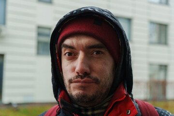 A man with an earnest expression shares his story while wearing a red beanie and cozy jacket indoors on a chilly day