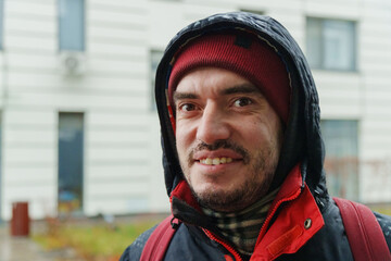 On a crisp day, a man in a red jacket stands outdoors, beaming with joy against the backdrop of contemporary architecture