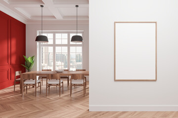 Blank framed poster on a white wall beside a dining area with red accents and wooden furniture. Minimalist design concept. 3D Rendering