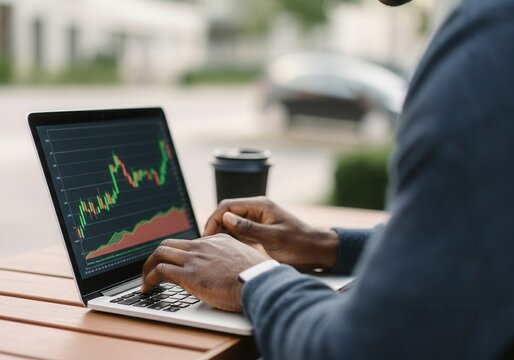 Young black man working as a trader analyzing charts on his laptop in an outdoor urban setting