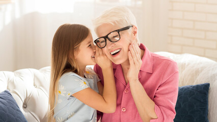 Family bonding. Little girl sharing secrets with her granny at home