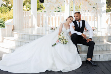 A bride and groom are sitting on a stone staircase, the bride holding a bouquet. Scene is romantic...