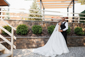 Fototapeta premium A bride and groom are posing for a picture in front of a brick wall. The bride is wearing a white dress and the groom is wearing a black vest. Scene is happy and celebratory