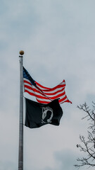 American flag and POW MIA flag flying in the wind with white sky background