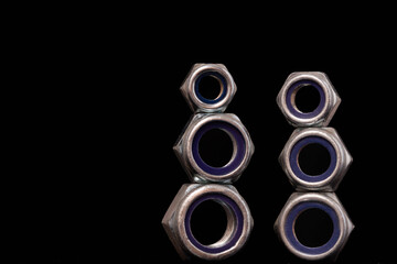 Steel nuts of different sizes on black background with reflecting dark surface. Close up macro shot with copy space