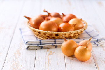 yellow onions in a basket on a white wooden table.