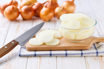 chopped yellow onions in a glass bowl on a white wooden table, selective focus.