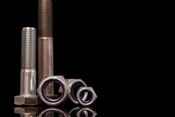 Steel nuts and bolts of different sizes on black background with reflecting dark surface. Close up macro shot with copy space