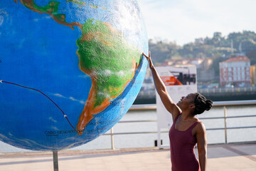 Young black woman touching giant earth globe promoting environmental awareness