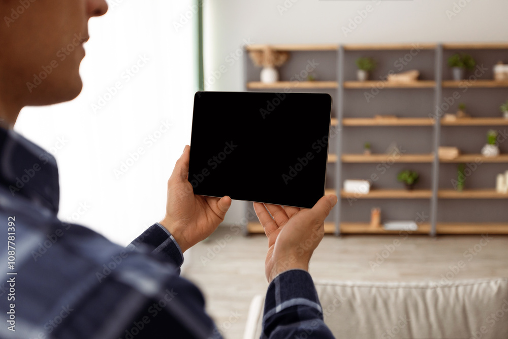 Poster guy holding digital tablet computer with blank screen over living room background standing indoors. 