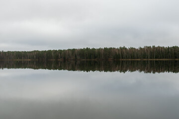 A serene lake mirrors the surrounding forest as low clouds hover overhead, creating a peaceful atmosphere in the early morning hours, inviting reflection and calm