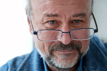 Close-up of a mature man with glasses and a gentle smile, wearing a denim shirt