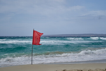 Bandera roja en la playa en un día ventoso con el mar agitado