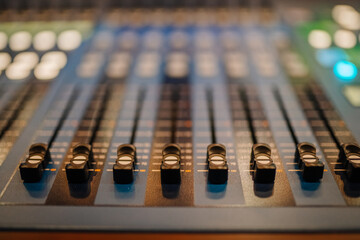 Close-up of audio mixing console faders with soft lighting, showing control knobs and sliders for...