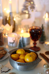 Various Christmas decorations, cookies, chocolate, nuts and tangerines, wine glasses and lit candles on the table. Holiday hygge at home. Selective focus.