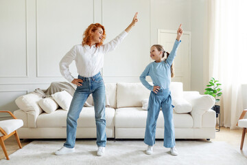 Joyful mom and teen girl having fun and dancing at home in living room interior, full length....