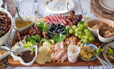 Fresh food for eating on a table for lunch. Cold plate of  various salad, cheese, ham, grapes and olives on board. Appetizer for meal in restaurant. Banner.