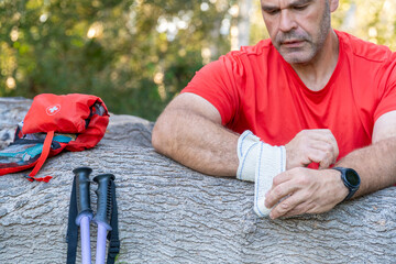 Hiker bandaging his injured wrist, leaning on a log, next to a first aid kit.