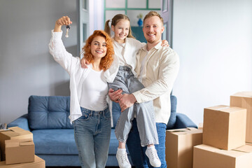 Family housing concept. Happy parents and daughter holding home keys in hands, celebrating moving day and smiling at camera