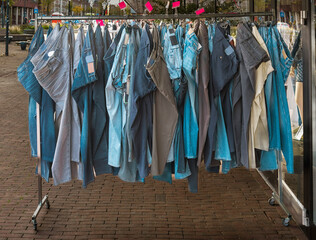 clothes rack with jeans is outside on the street next to a shop