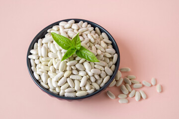 Bowl full of white beans over pastel pink background. Vegetarian protein, organic farm products, harvesting concept. Ingredient for cooking baked beans, bean soup, bean pies.