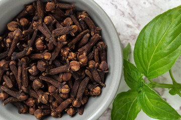 Organic cloves spice in a small bowl macro. Close-up of dry clove buds in a gray ceramic bowl and basil leaf. Cooking, herbal medicine and spice concept.