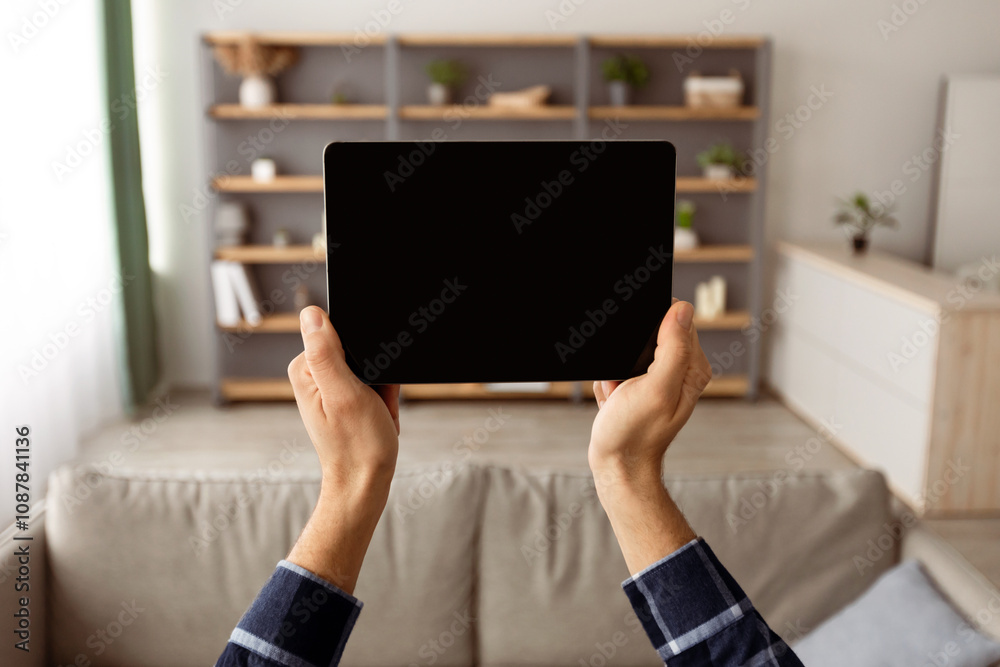Poster Male Hands Holding Digital Tablet With Blank Screen Mockup For Website Advertisement Standing At Home. Guy Showing Computer Display Template Over Domestic Living Room Background. Selective Focus
