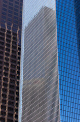 A close-up view of modern office buildings in downtown Los Angeles. The buildings feature sleek glass facades that reflect the surrounding structures, creating an intricate pattern of reflections.