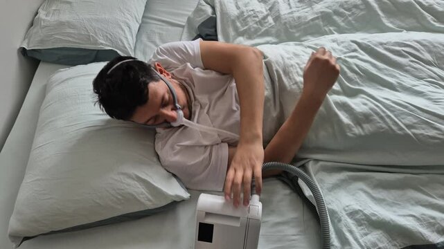 A man in his mid-thirties with sleep apnea sleeps using a nasal mask and CPAP device in a bed in his house