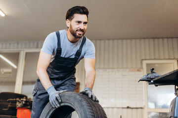 Portrait of professional, bearded man wearing uniform, holding tire, working in service station.