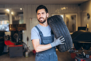 Bearded man wearing uniform, professional repairman holding tire, wheels working in service station